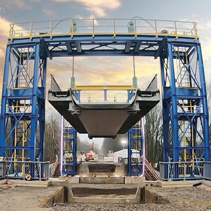 Eine Brücke hängt zwischen zwei blauen Montagetürmen und wird hinaufgezogen.